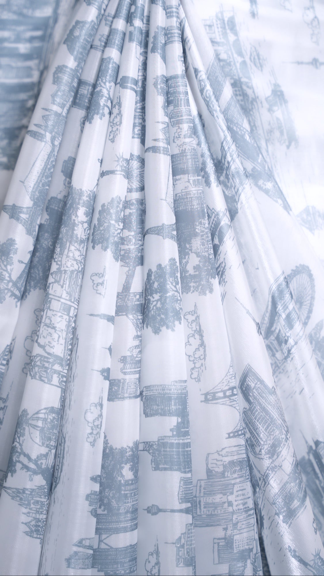 Close up of front pleats on a draped white organza saree with a grey satin border and grey printed city skylines throughout.