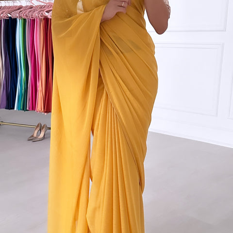 Model taking a selfie wearing a rose gold sequin crop top, draped in a bright yellow saree. The saree has silver threading sewn throughout, giving a shimmery appearance.