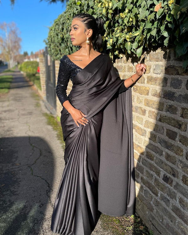 Model wearing a 3/4 sleeve black v-neck sequin crop top and draped in a black satin silk saree.