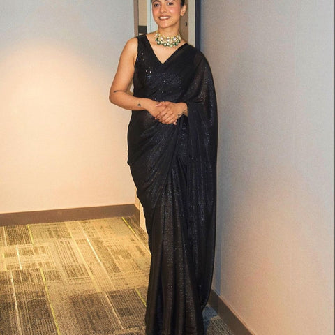 Model wearing a sleeveless black sequin crop top, draped in a black saree. The saree has silver threading sewn throughout, giving a shimmery appearance.