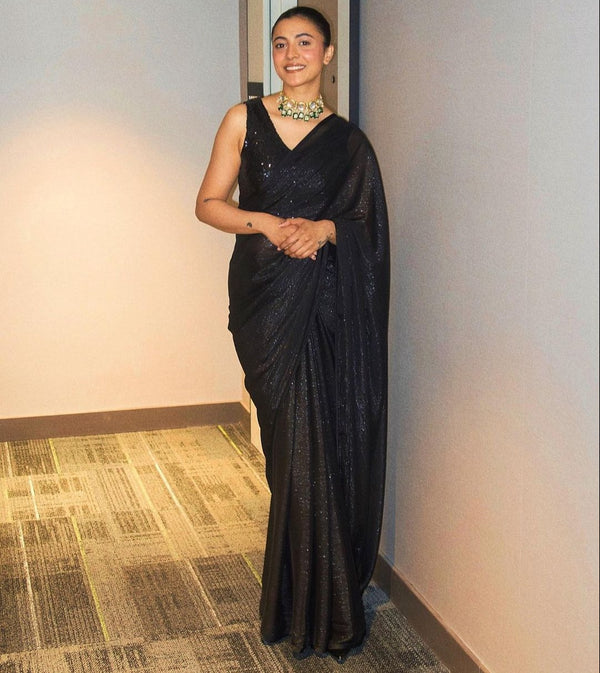 Model wearing a sleeveless black sequin crop top, draped in a black saree. The saree has silver threading sewn throughout, giving a shimmery appearance.