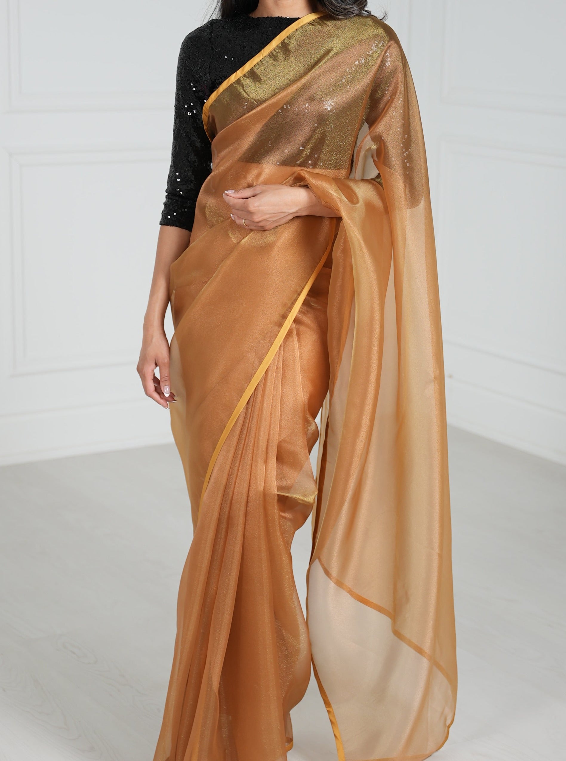 Model draped in a copper organza saree with copper satin border. Model is also wearing a black 3/4 sleeve sequin crop top.