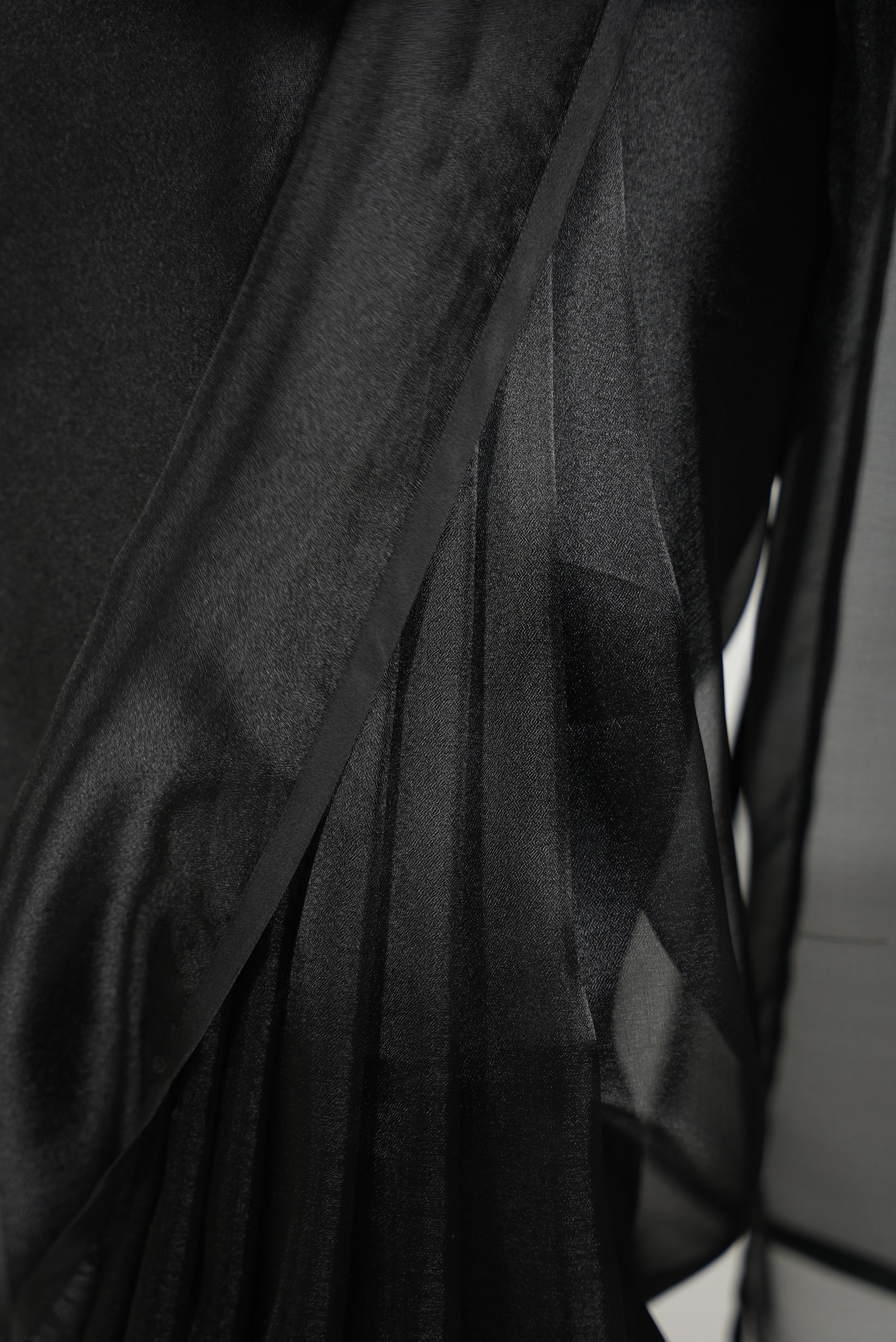 Close up of front pleats on a black organza saree with black satin border. 