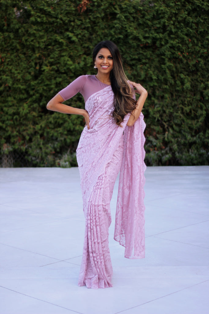 Model draped in a lilac purple lace saree with scalloped edging. Model is also wearing a mauve purple short sleeve crop top.
