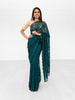 Model draped in an emerald green lace saree with scalloped edging. Model is also wearing a short sleeve champagne colored crop top and saree petticoat underneath in matching emerald green color.