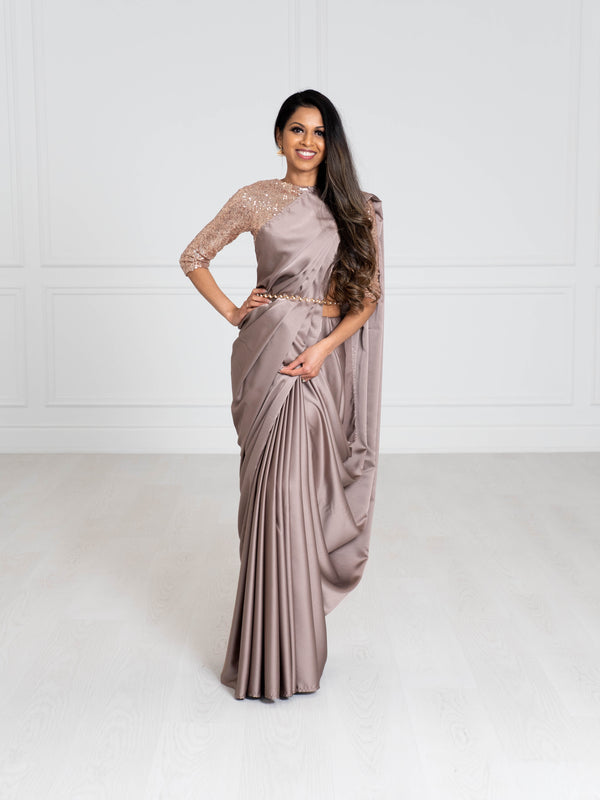 Model wearing a 3/4 sleeve rose gold sequin crop top and draped in a mauve grey satin silk saree. Model is also wearing a gold waist chain with pearls.