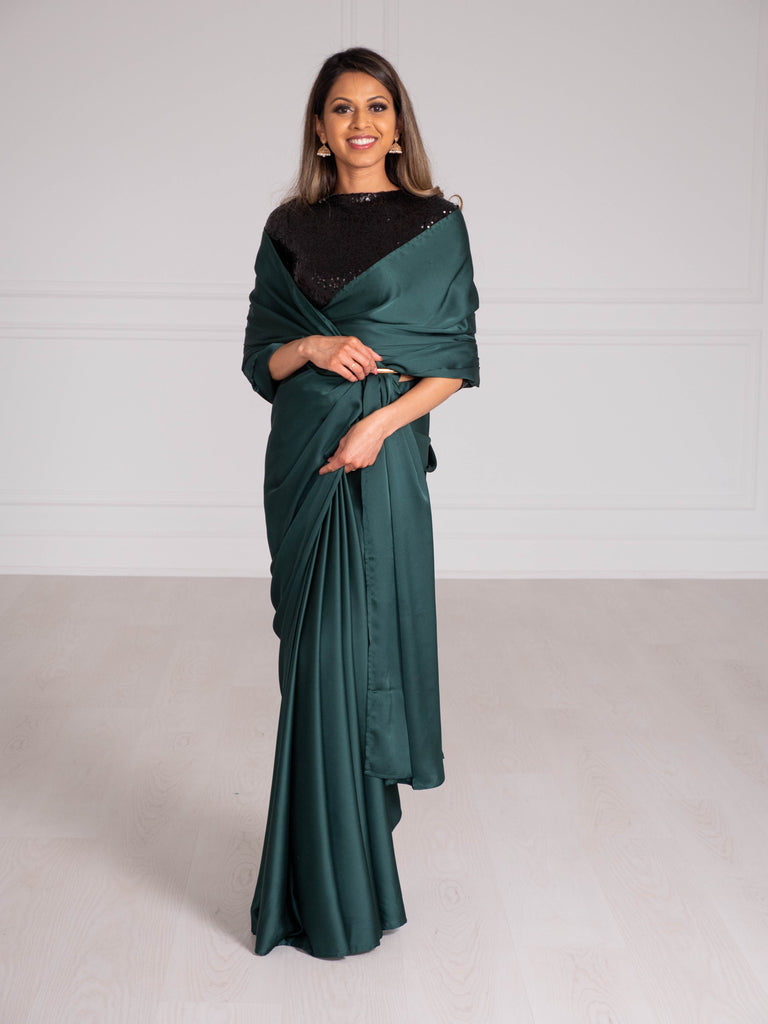 Model wearing a 3/4 sleeve black sequin crop top and an off-shoulder draped emerald green satin silk saree.