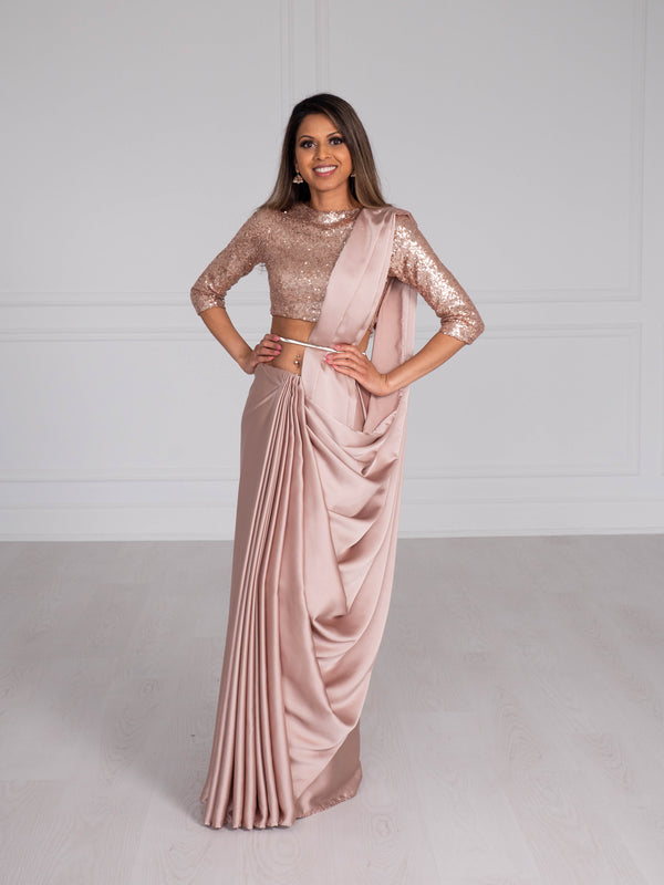 Model wearing a 3/4 sleeve rose gold sequin crop top and draped in a rose gold satin silk saree. Model is also wearing a silver waist chain.