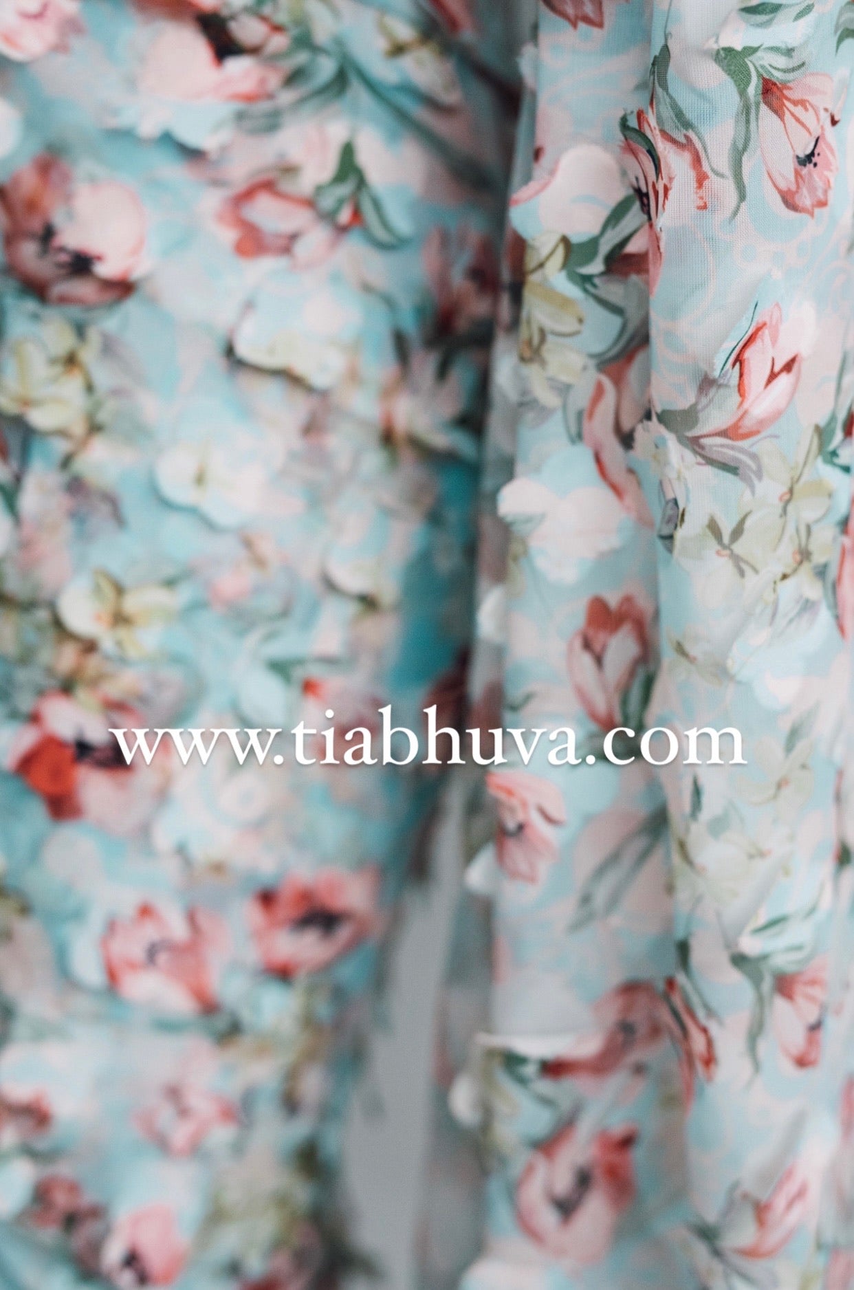 Detailed close up of a lightweight pale blue saree with a red, green, and pink floral print and 3D petals. 